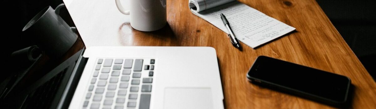 MacBook Pro, white ceramic mug,and black smartphone on table